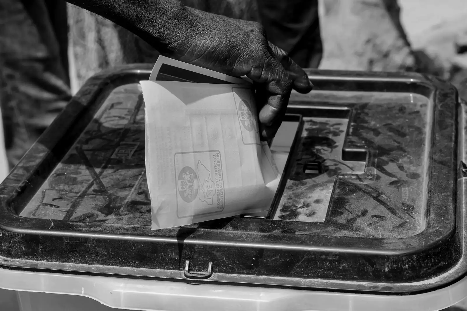 A hand pushes a folded ballot paper into the slot of a plastic ballot box.